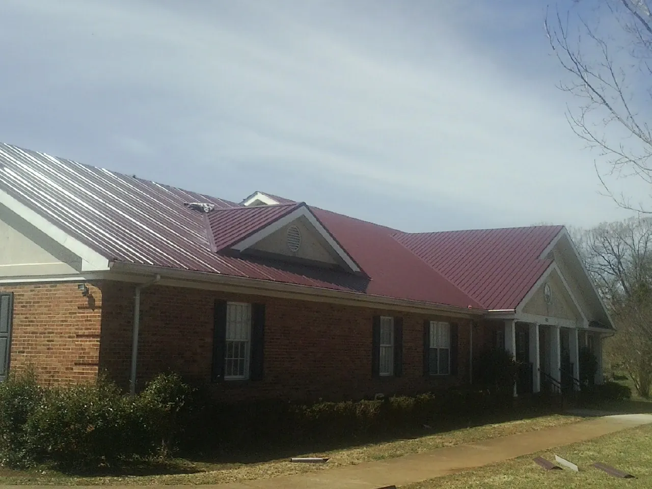 Red metal roof with gabled entries on a long brick building, from a Hail Damage Roof Repair job in Weymouth
