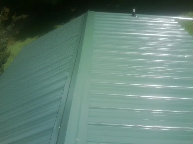 New green metal panels meeting at the ridge of a roof — Flat Roof Repair work by our crew in Weymouth