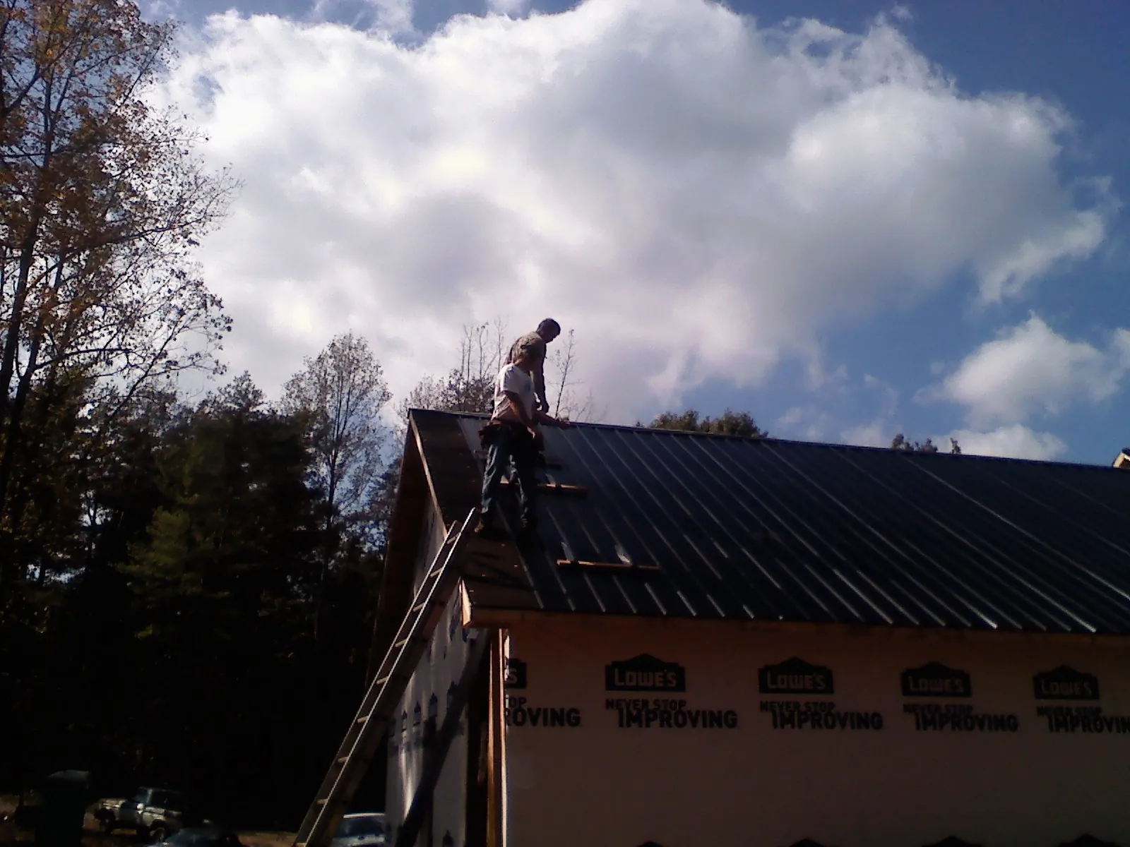 Roofer fastening dark metal panels high against a cloudy sky, from a Roof Inspection job in Weymouth