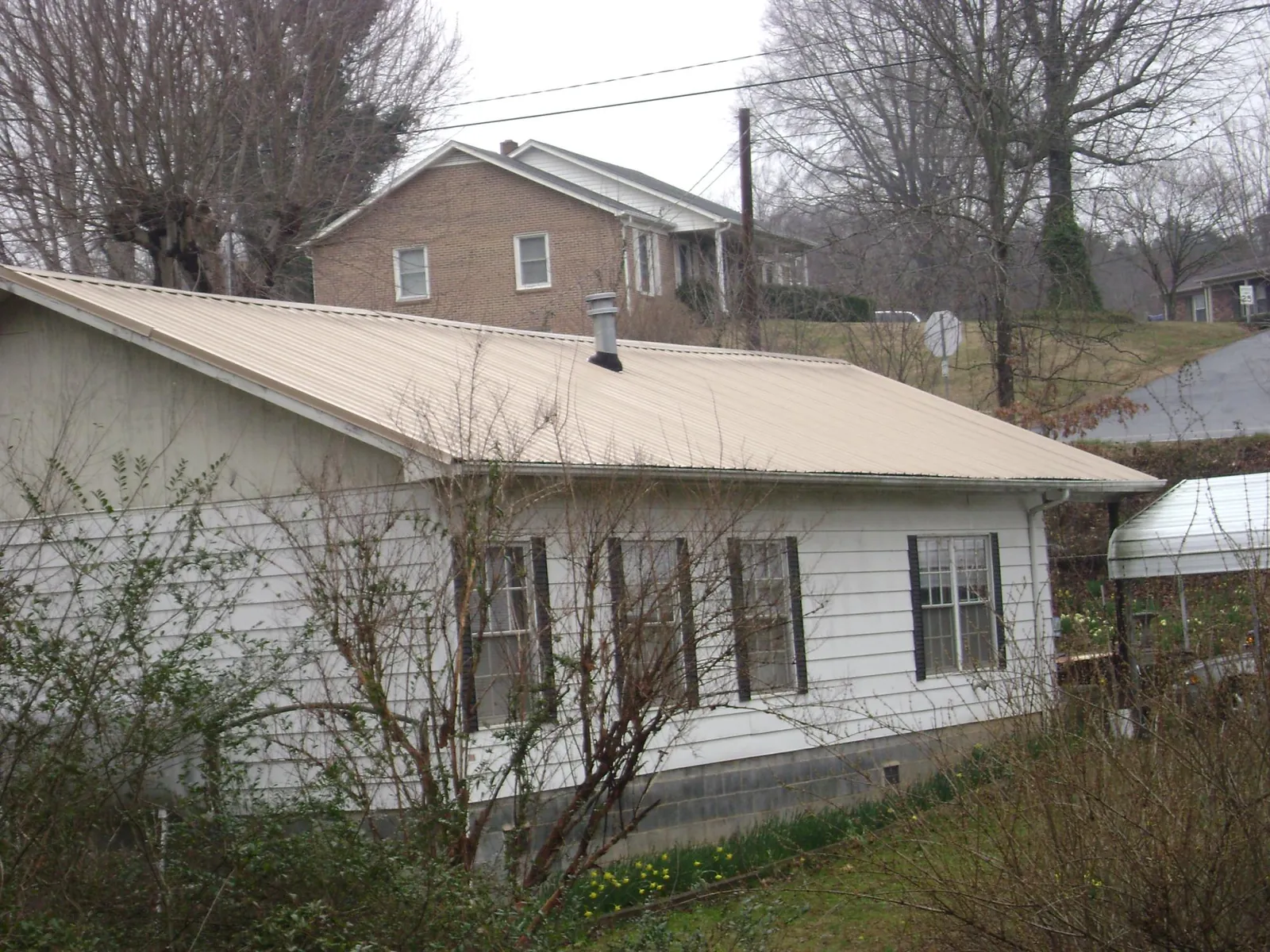 Tan metal roof on a white sided house set into a hillside — Commercial Roofing by Roofing Brothers in Weymouth